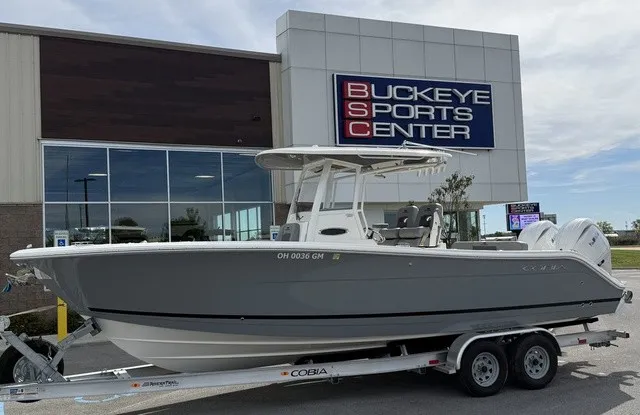 Slide: The Image of A gray 2024 Cobia 280 Center Console boat on a trailer outside a sports center. - 1