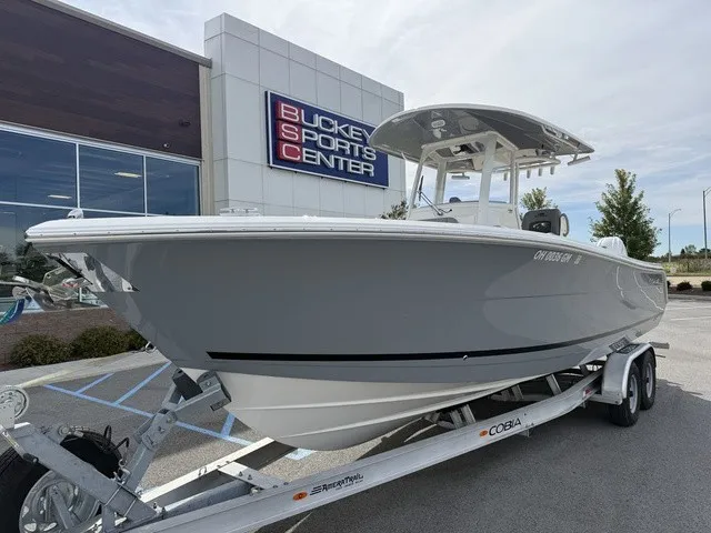 Slide: The Image of A gray 2024 Cobia 280 Center Console boat on a trailer outside a sports center. - 2