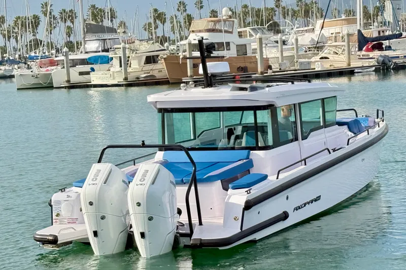 Slide: The Image of 2025 Axopar 37 XC Cross Cabin boat docked in a marina with twin outboard engines. - 2