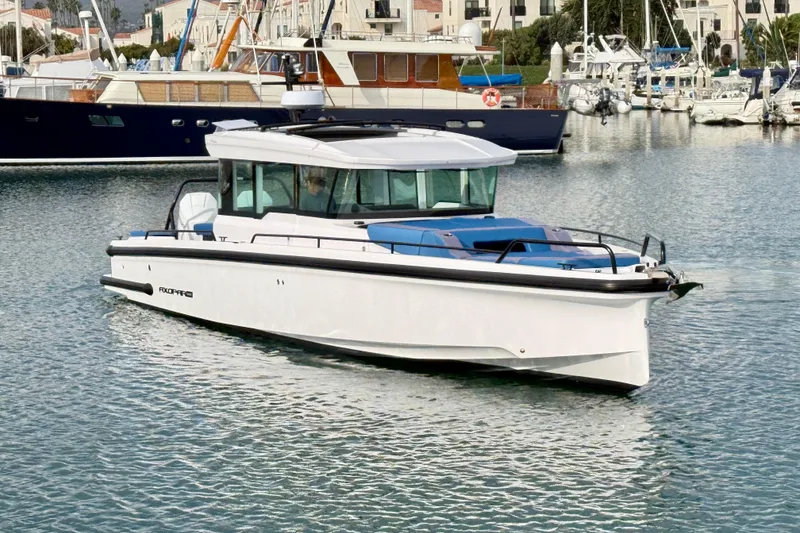 Slide: The Image of 2025 Axopar 37 XC Cross Cabin boat in a marina, surrounded by other vessels. - 11