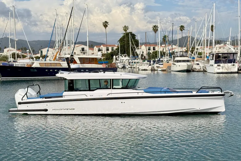 Slide: The Image of 2025 Axopar 37 XC Cross Cabin boat docked in a marina with sailboats. - 10