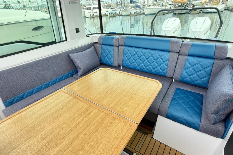 Slide: The Image of 2025 Axopar 37 XC Cross Cabin interior with blue quilted seating and wooden table. - 14