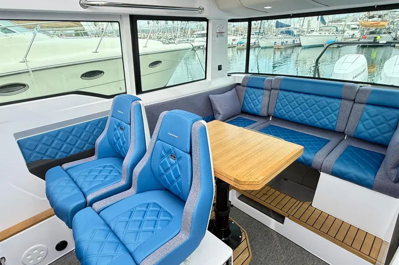 Slide: The Image of 2025 Axopar 37 XC Cross Cabin interior with blue seating and wooden table. - 12