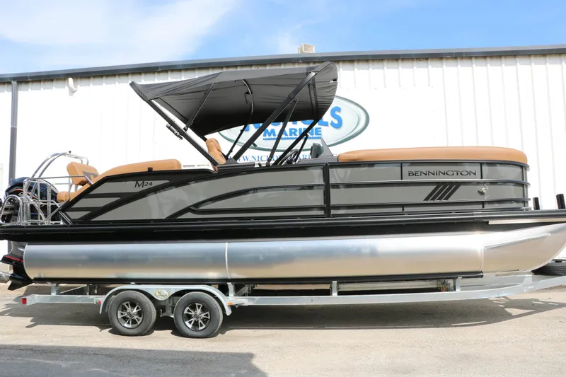 Slide: The Image of A 2027 Bennington 24 MSL Tri Toon on a trailer, featuring a black canopy and brown seating. - 2