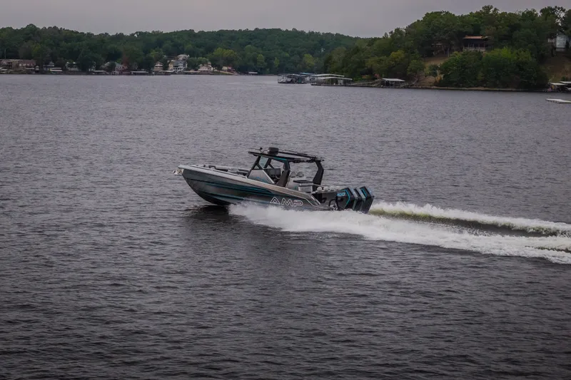 Slide: The Image of 2025 AMP 333 CC boat cruising on a lake with lush green shoreline. - 73