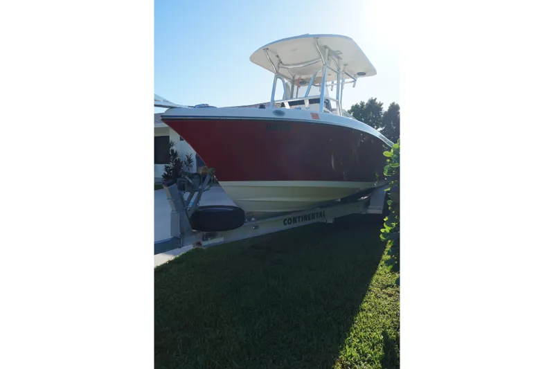 Slide: The Image of 2014 Century 2200 Center Console boat on trailer, red hull, parked on grass. - 14