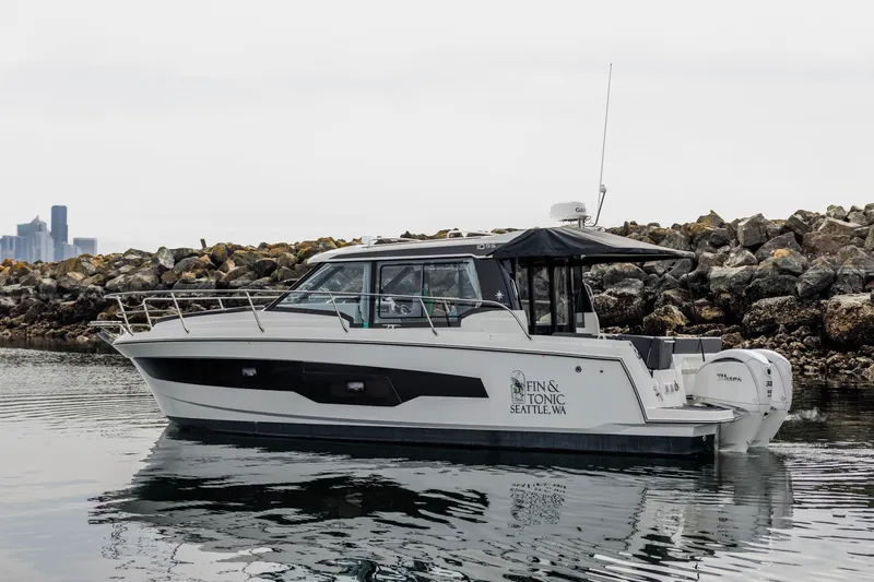The Image of A 2024 Jeanneau NC 1095 Coupe is on the water near a rocky shoreline. - 0