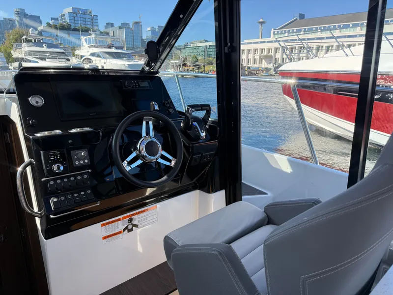 Slide: The Image of The cockpit of the 2024 Jeanneau NC 1095 Coupe features modern instruments and a comfortable seat overlooking the harbor. - 15