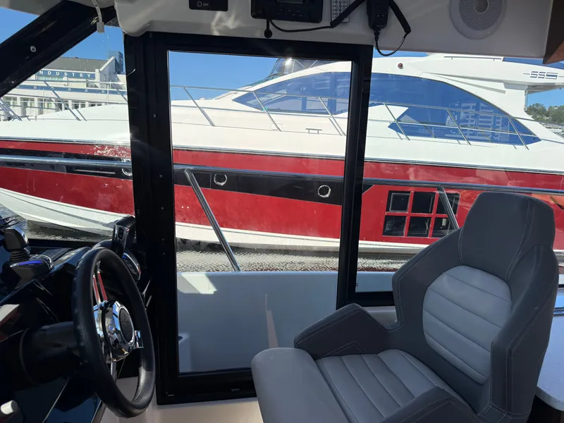Slide: The Image of Interior view of a 2024 Jeanneau NC 1095 Coupe with a gray seat and view of a red boat. - 16