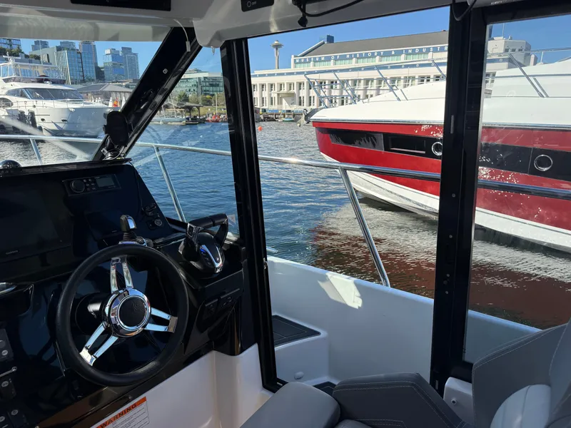 Slide: The Image of The cockpit of a Jeanneau NC 1095 Coupe overlooking a harbor and a red boat. - 36