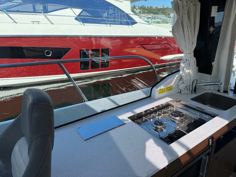 Slide: The Image of The 2024 Jeanneau NC 1095 Coupe's galley features a stove and sink with a view of the water. - 17