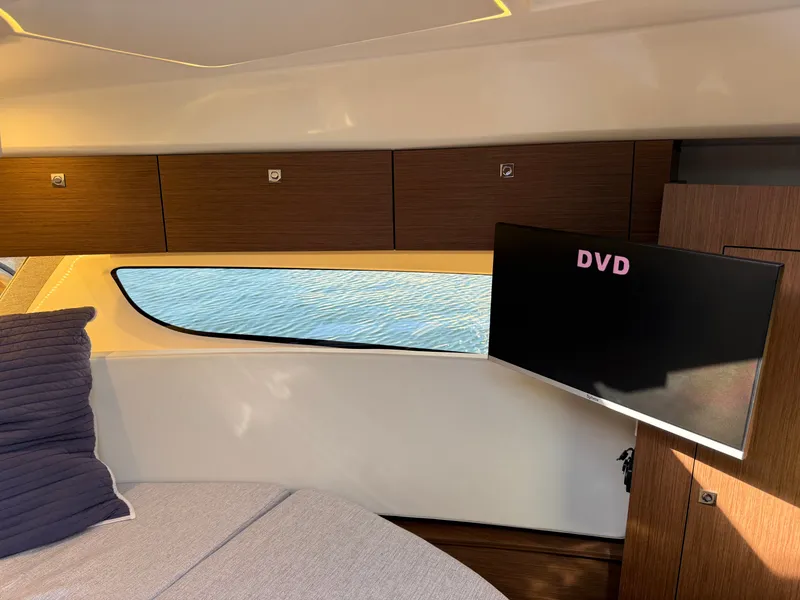 Slide: The Image of Interior of a 2024 Jeanneau NC 1095 Coupe featuring a sofa, window, and television. - 24