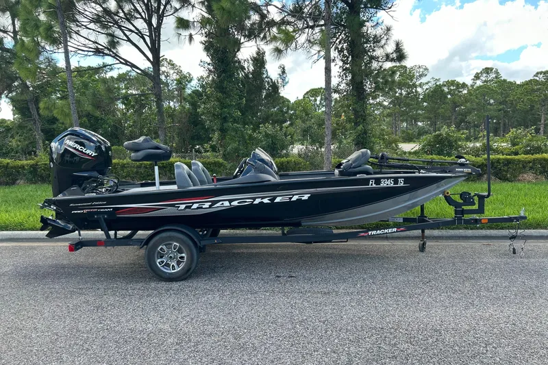 The Image of 2024 Tracker Pro Team 175 TXW boat on trailer, parked roadside with trees in background. - 0