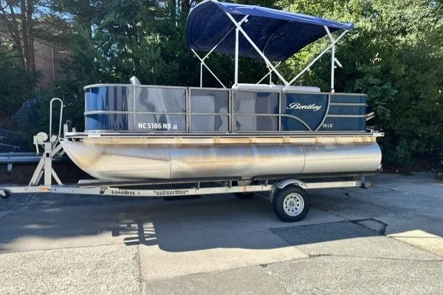 The Image of 2023 Bentley 180 LE pontoon boat on trailer with blue canopy, parked outdoors. - 0