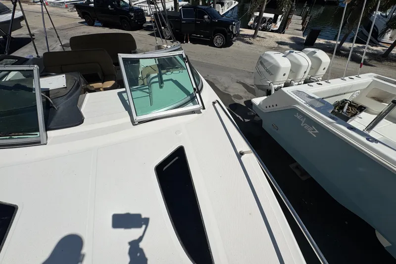 Slide: The Image of 2018 Sea Ray Sundancer 260 boat docked, featuring open deck and nearby parked vehicles. - 22