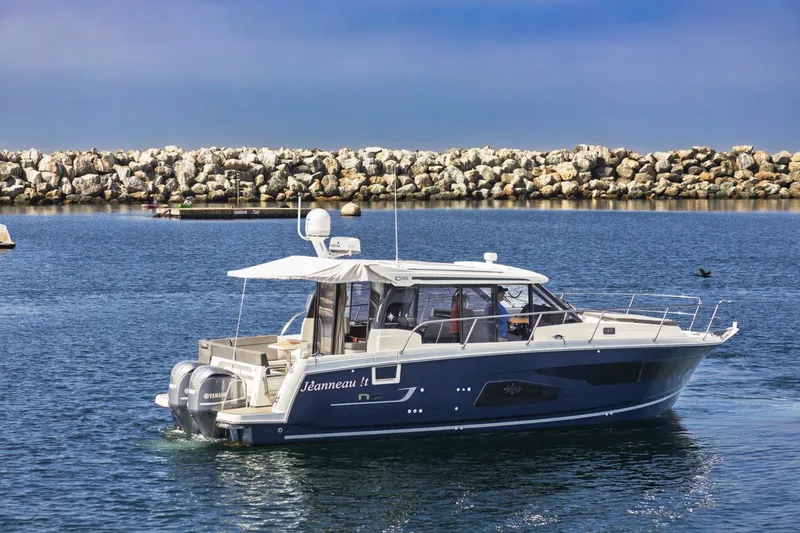 The Image of 2020 Jeanneau NC 1095 boat cruising in calm waters near a rocky shoreline. - 0