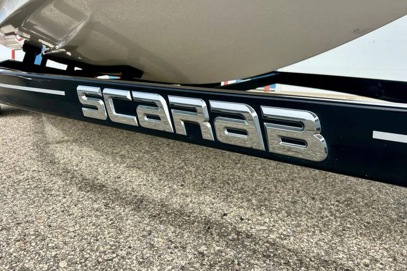 Slide: The Image of 2022 Scarab 215 ID boat trailer with chrome logo on pavement. - 61
