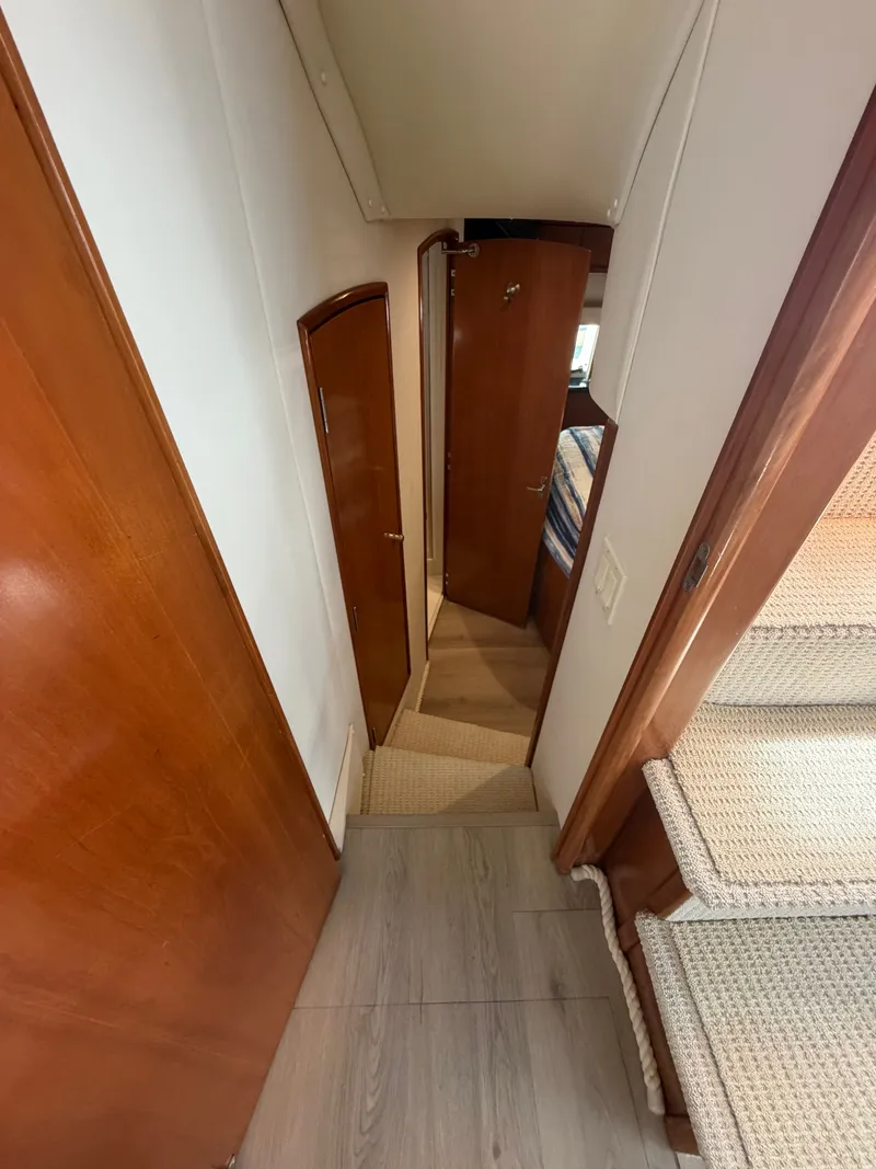 Slide: The Image of A narrow hallway in a yacht with wooden doors and carpeted flooring. Stairs lead upwards. - 45