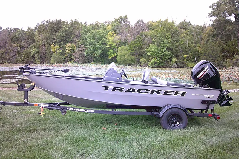 The Image of 2027 Tracker Super Guide V-16 SC boat on trailer by a scenic lake. - 0