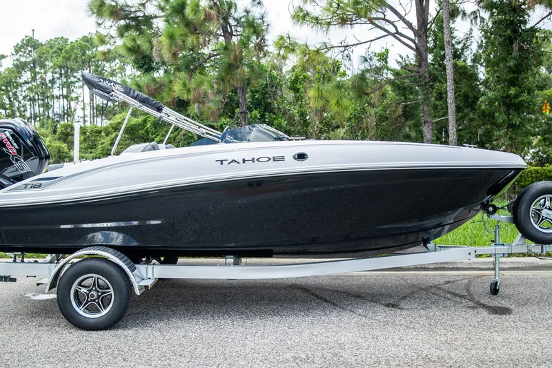 Slide: The Image of 2027 Tahoe T18 boat on trailer, parked on road with trees in background. - 1