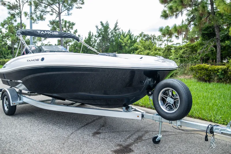 Slide: The Image of 2027 Tahoe T18 boat on trailer, parked on a road near lush greenery. - 2