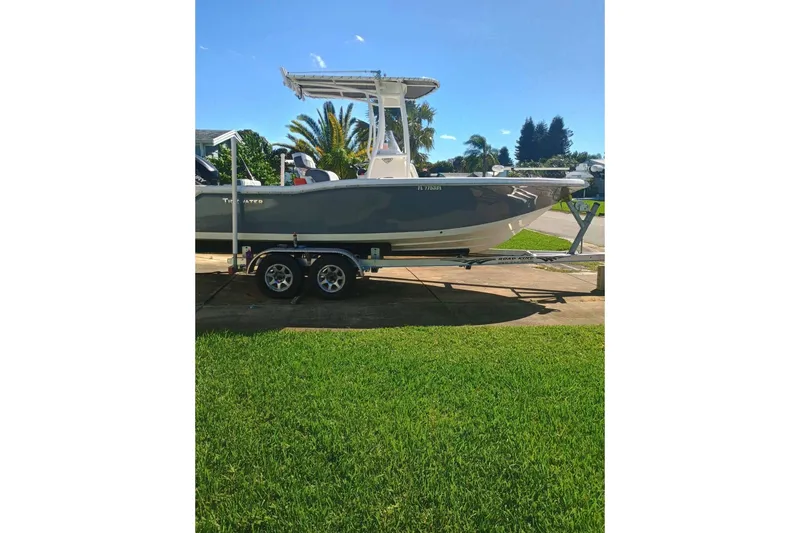 Slide: The Image of 2019 Tidewater 210 CC Adventure boat on trailer, parked on grass under clear sky. - 3