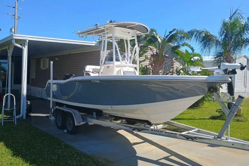 Slide: The Image of 2019 Tidewater 210 CC Adventure boat on trailer, parked beside a house with palm trees. - 1
