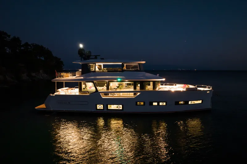 Slide: The Image of Luxurious Sirena 78 yacht illuminated at night, reflecting on calm water, 2027 model. - 2