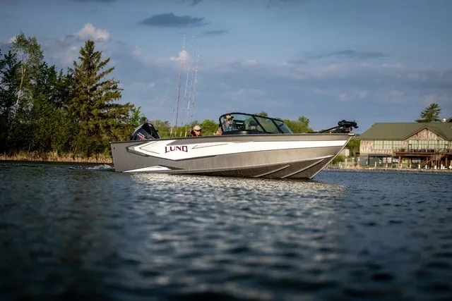 The Image of A Lund 2075 Fisherman boat cruising on a calm lake with a wooded shoreline in the background. - 2