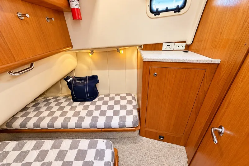 Slide: The Image of 2001 Mainship 390 Trawler cabin interior with checkered bedding and wooden cabinetry. - 29