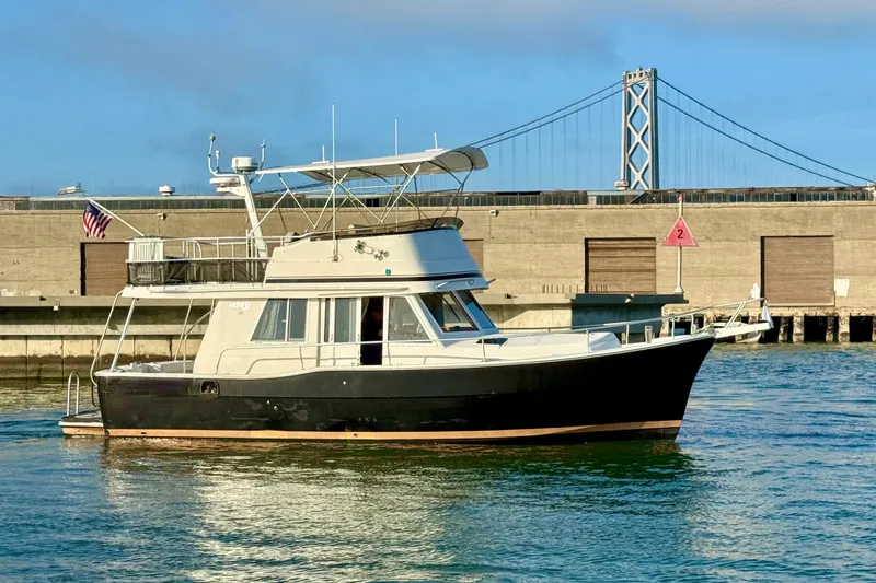 Slide: The Image of 2001 Mainship 390 Trawler on water near bridge and industrial backdrop. - 3
