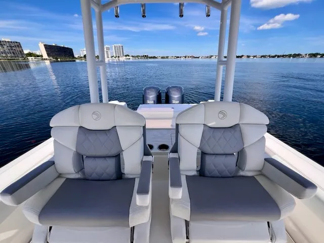 Slide: The Image of Two luxurious seats on a 2018 Edgewater 320CC boat, overlooking calm water and cityscape in the background. - 25