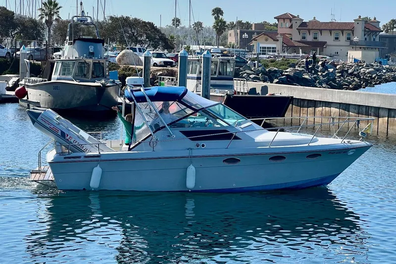 Slide: The Image of 1985 Tiara 25 boat docked in a marina with scenic waterfront background. - 1