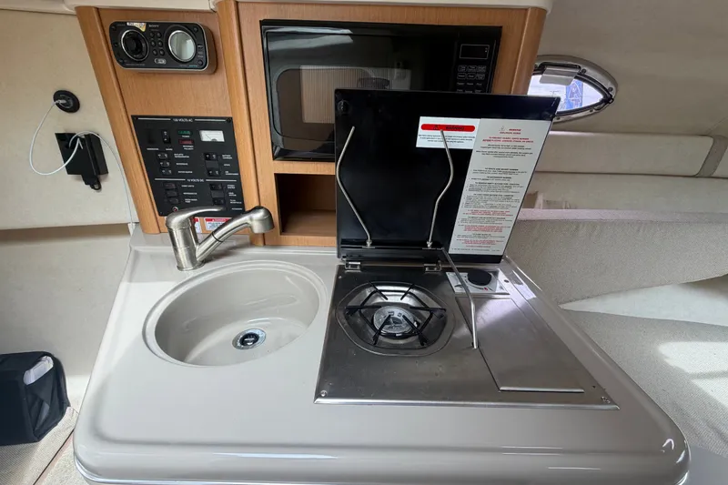 Slide: The Image of 2009 Sea Ray 240 Sundancer interior with kitchenette, featuring sink, stove, and control panel. - 66