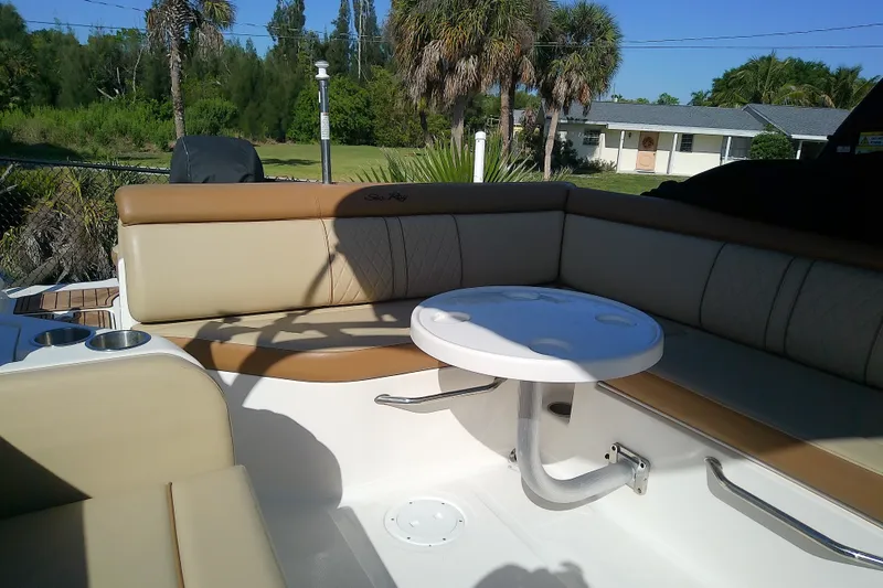 Slide: The Image of 2015 Sea Ray SDX 270 Outboard boat interior with seating and table, surrounded by lush greenery. - 18