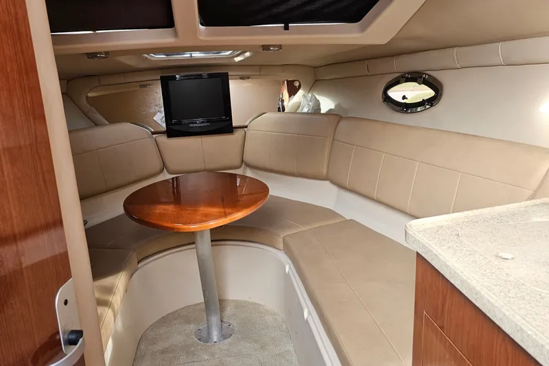 Slide: The Image of 2008 Regal 2565 Express Cruiser interior with beige seating, wooden table, and mounted TV. - 1