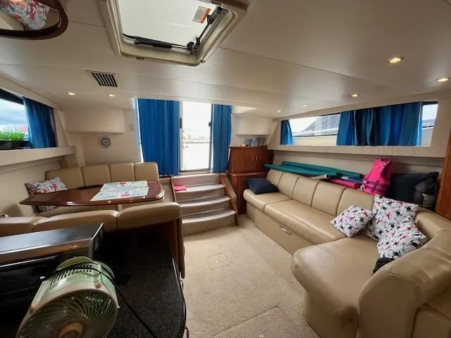 Slide: The Image of Der Innenraum einer Carver 360 Mariner von 2005 zeigt eine gemütliche Sitzecke mit beigen Sofas und blauen Vorhängen. - 32