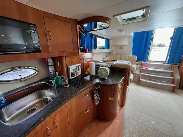 Slide: The Image of Die Innenansicht einer Carver 360 Mariner von 2005 zeigt eine gut ausgestattete Küche mit Spüle, Mikrowelle und Stauraum. Ein Sitzbereich mit blauen Vorhängen ist ebenfalls sichtbar. - 41
