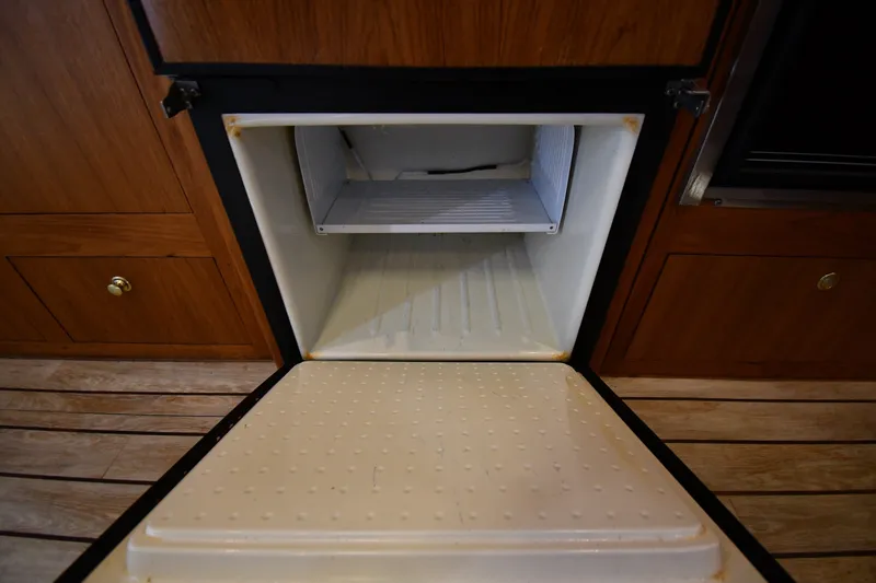Slide: The Image of Open refrigerator inside a 2000 Mainship 390 Trawler, showcasing wooden cabinetry. - 45