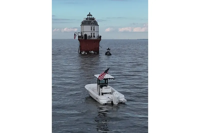 Slide: The Image of 2024 Caymas 281 HB boat near a lighthouse on calm waters, American flag displayed. - 2