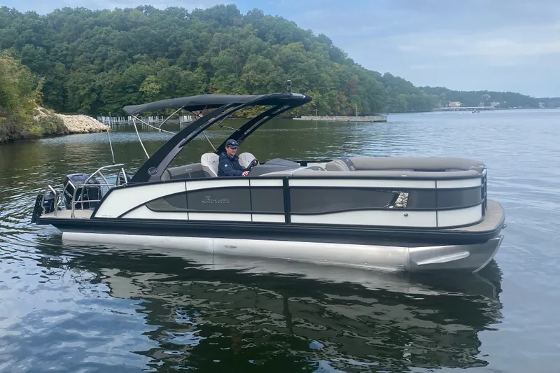 The Image of 2023 Barletta Lusso 25UCA pontoon boat on a serene lake with lush green backdrop. - 1