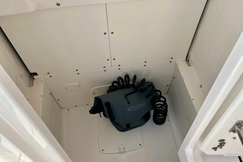 Slide: The Image of 2027 Robalo R250 Center Console storage compartment with coiled hose and branded bag. - 23