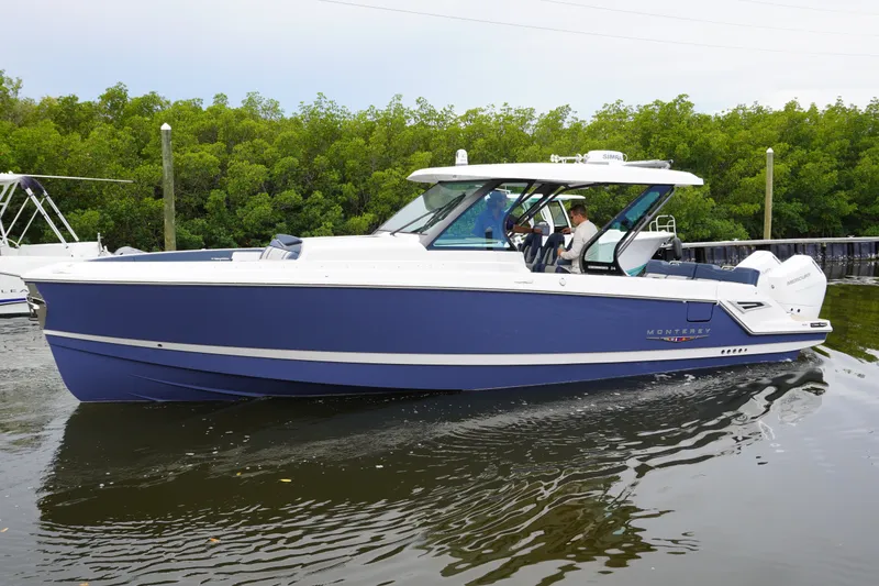 The Image of 2027 Monterey Elite 34 OB boat cruising on calm water near lush greenery. - 2