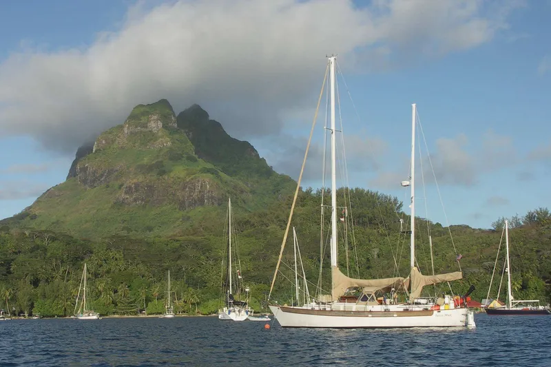 Slide: The Image of Sailboats anchored near lush green mountain under cloudy sky, featuring Passport Hoyt 45, 1982 model. - 5