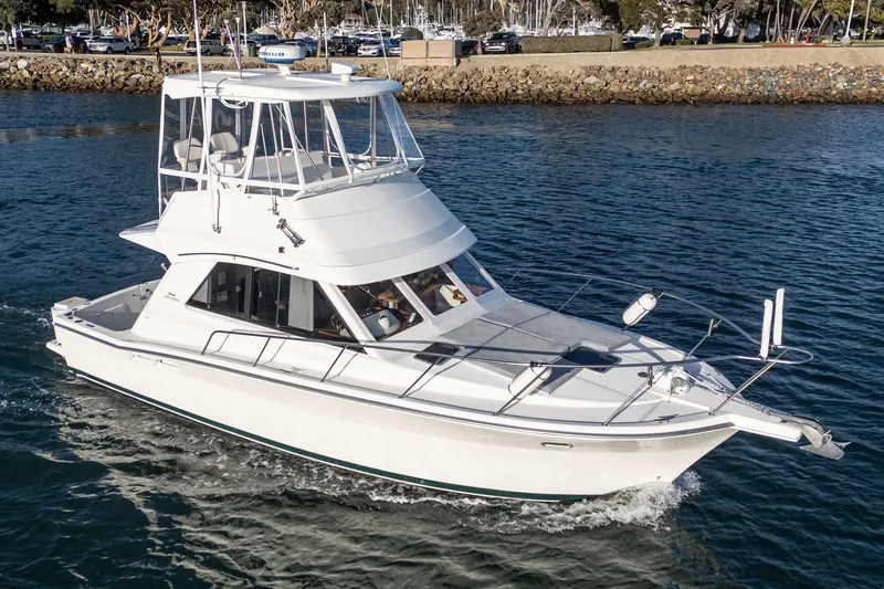 Slide: The Image of 1998 Riviera 34 Convertible yacht cruising on calm waters near a marina. - 55