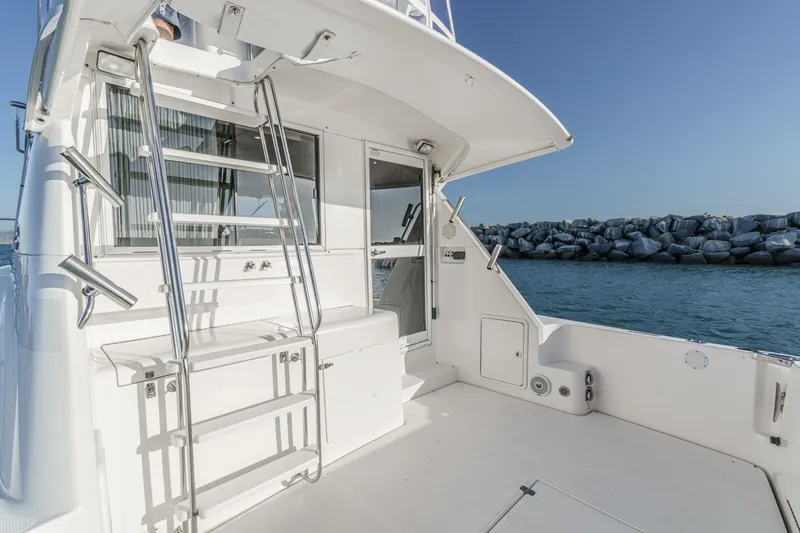 Slide: The Image of 1998 Riviera 34 Convertible yacht deck with ladder, overlooking calm waters and rocky shoreline. - 16