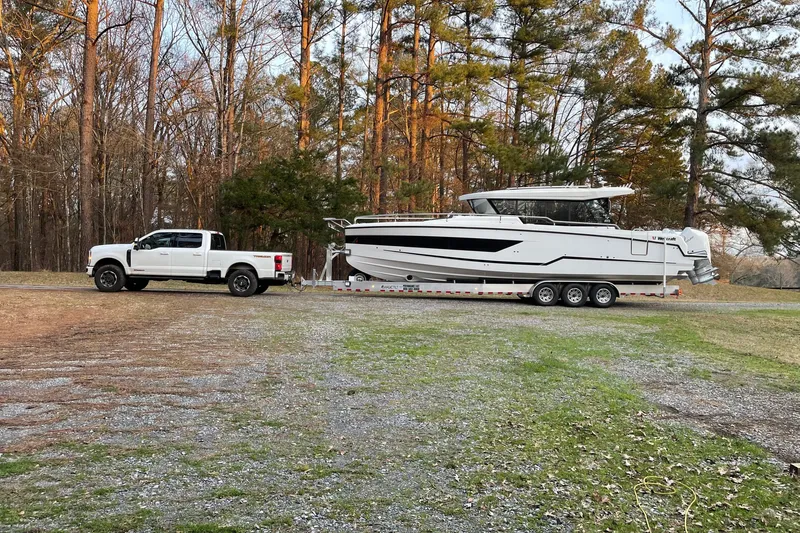Slide: The Image of 2024 Wellcraft 38 Explorer boat on trailer, towed by a white truck in a wooded area. - 2