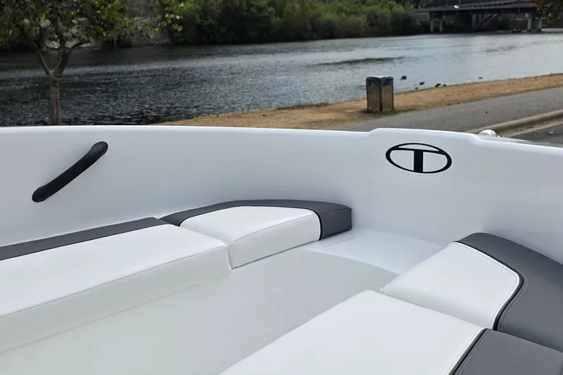 Slide: The Image of 2027 Tahoe T16 boat interior with white and gray seating by a serene lakeside. - 69