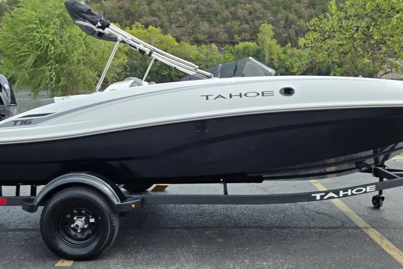 The Image of 2027 Tahoe T16 boat on trailer, parked outdoors with lush greenery background. - 0