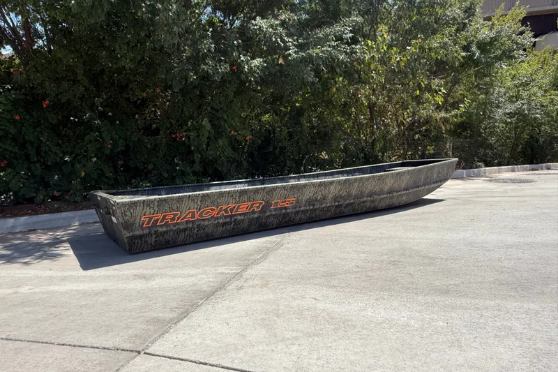 Slide: The Image of 2027 Tracker Grizzly 15 Jon boat on pavement, surrounded by greenery. - 29